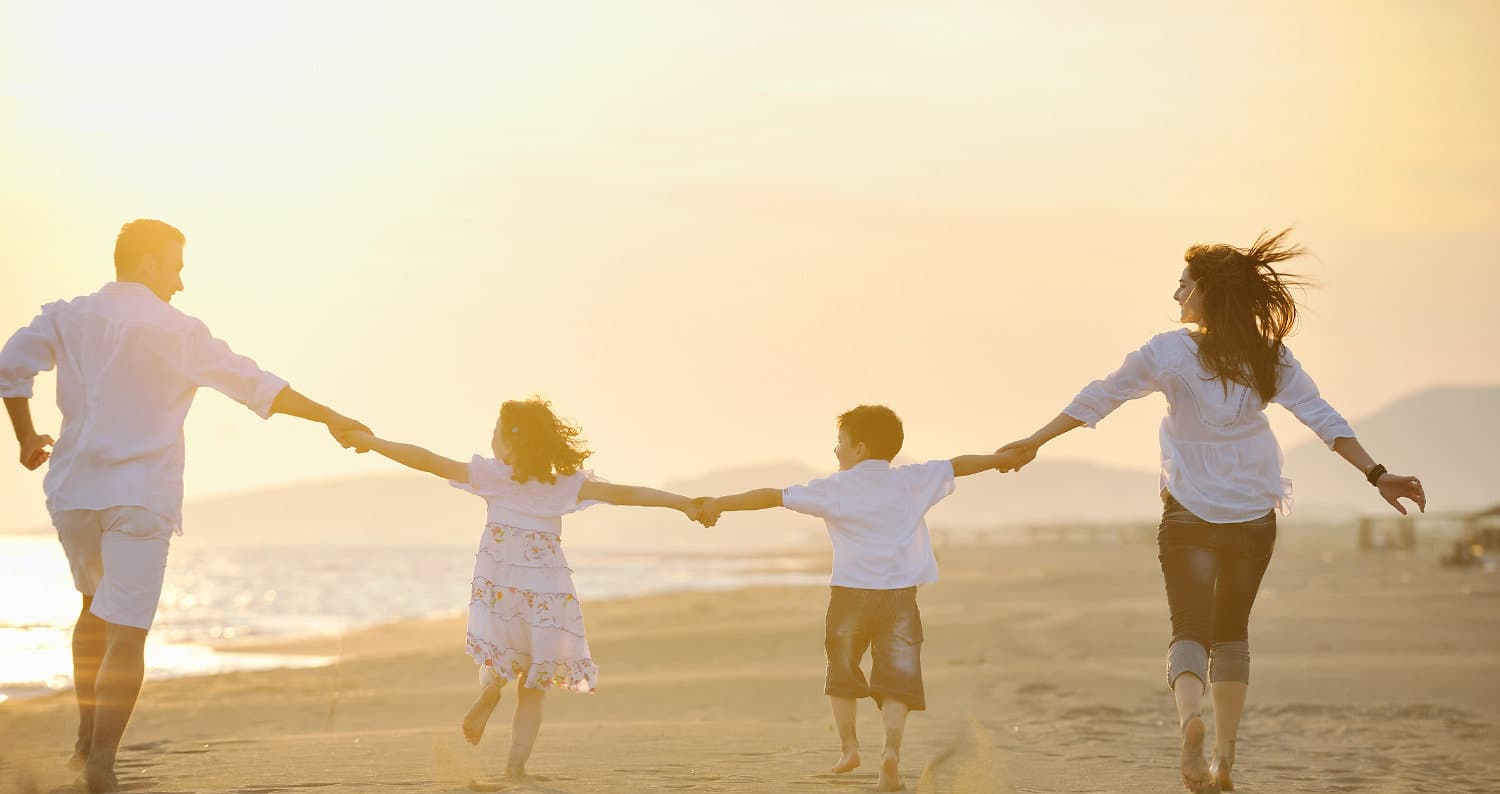 A family of four holding hands as they run along the beach at sunset