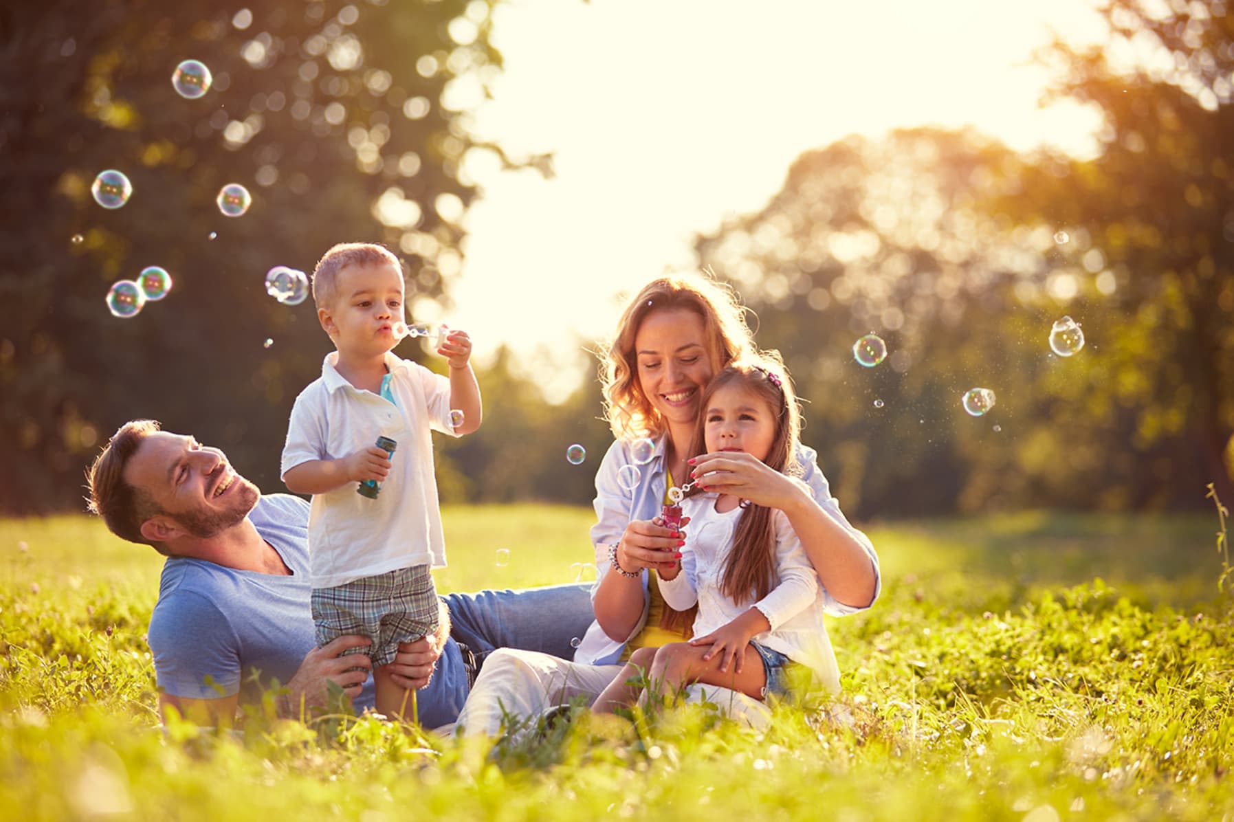 A family of four enjoying bubbles together on a sunlit lawn at golden hour