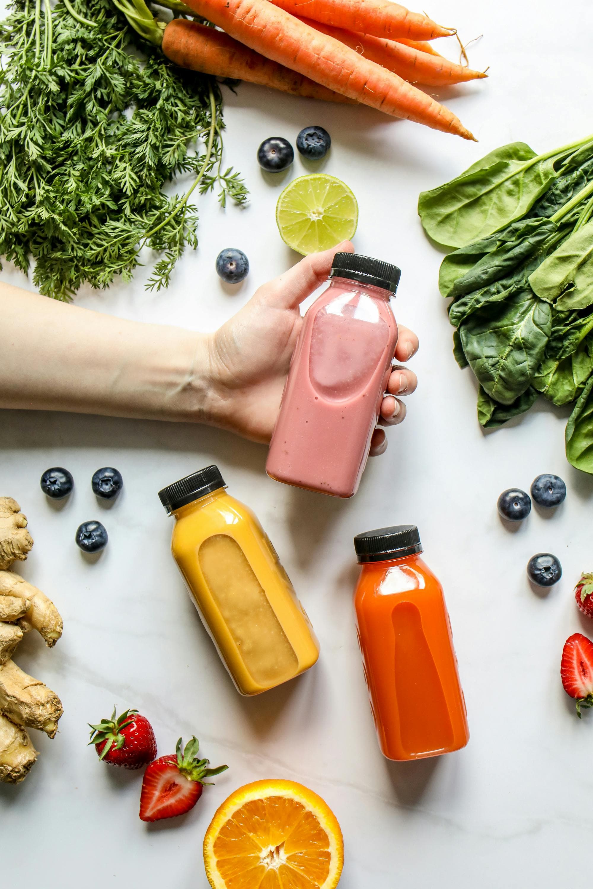 Fresh fruit and vegetable smoothies — strawberry, mango and carrot — surrounded by detox ingredients including spinach, ginger, lime and blueberries from the 30 Days programme at Vibrant Life Centre