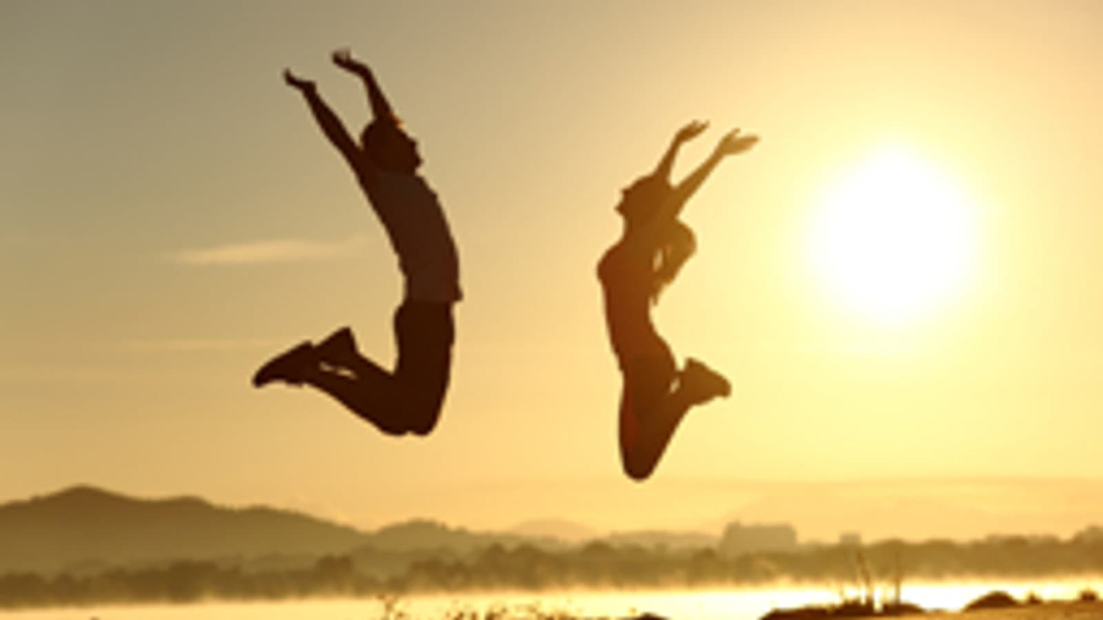 Two people silhouetted jumping at sunset — vitality and joy