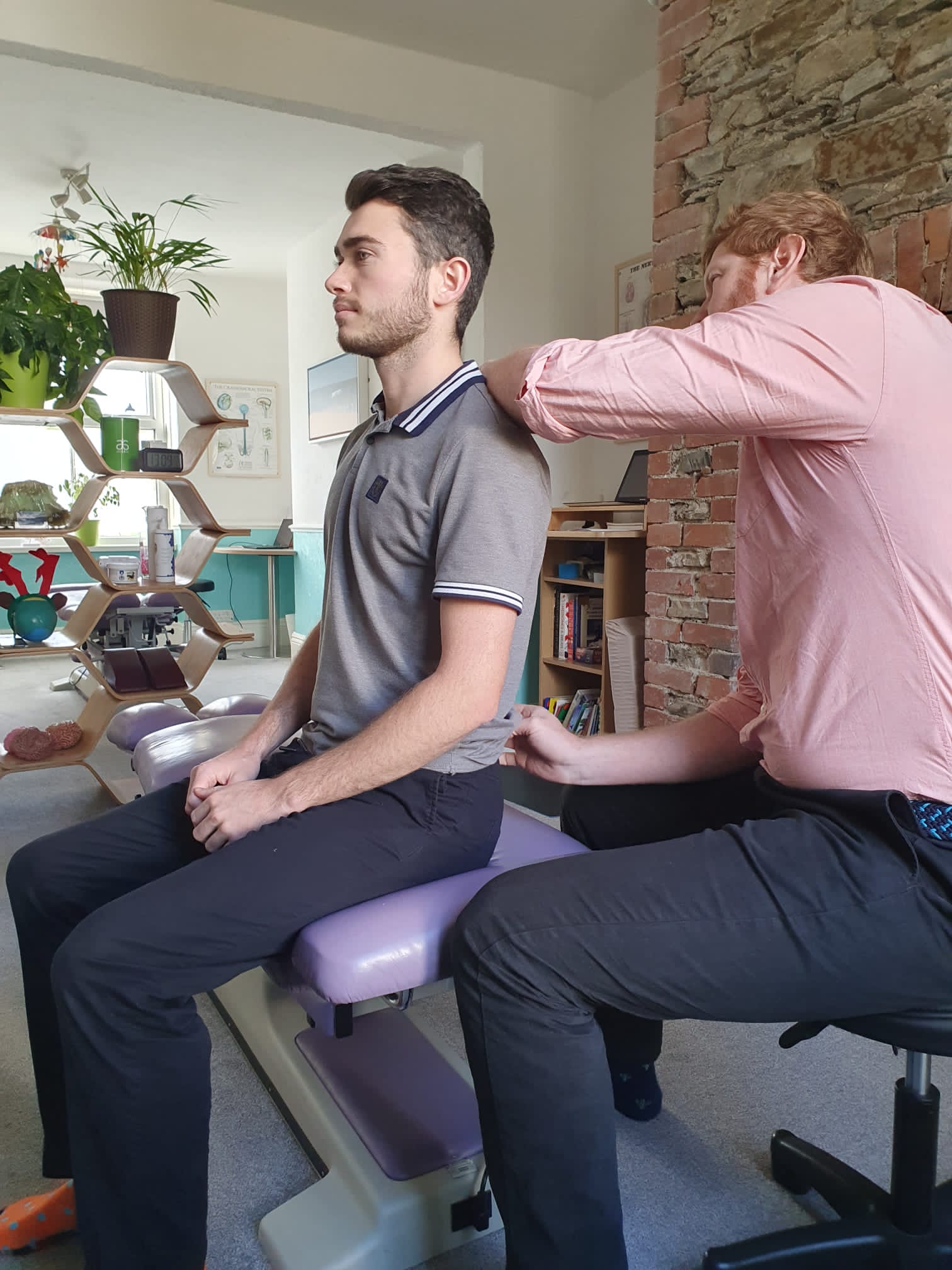 Will Tucker assessing a seated guest in the Vibrant Life consulting room, with teal wainscoting and honeycomb shelving visible