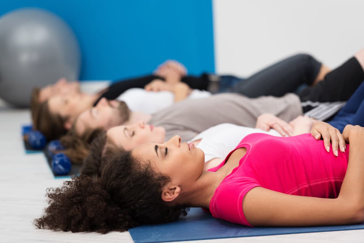 A group of four guests in relaxation pose on yoga mats, eyes closed, calm at-home recovery practice